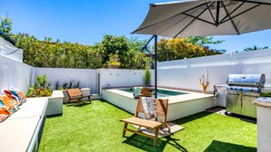 Een achtertuin met een zwembad, een barbecue en een zitgedeelte met stoelen en een parasol.