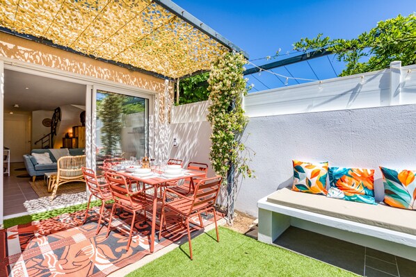 A patio with a table and chairs, a bench with cushions, and a covered area with climbing plants.