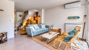 Een woonkamer met een blauwe bank, rieten stoelen, een salontafel en een trap, met een bordje waarop 'WAIMEA BAY' staat.