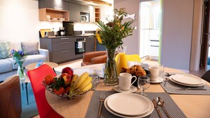 Un coin repas avec une table mise pour le petit-déjeuner, un vase rempli de fleurs et, au fond, une cuisine.
