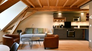 Un espace de vie de style loft comprenant une cuisine, des poutres en bois, un canapé et un coin repas.