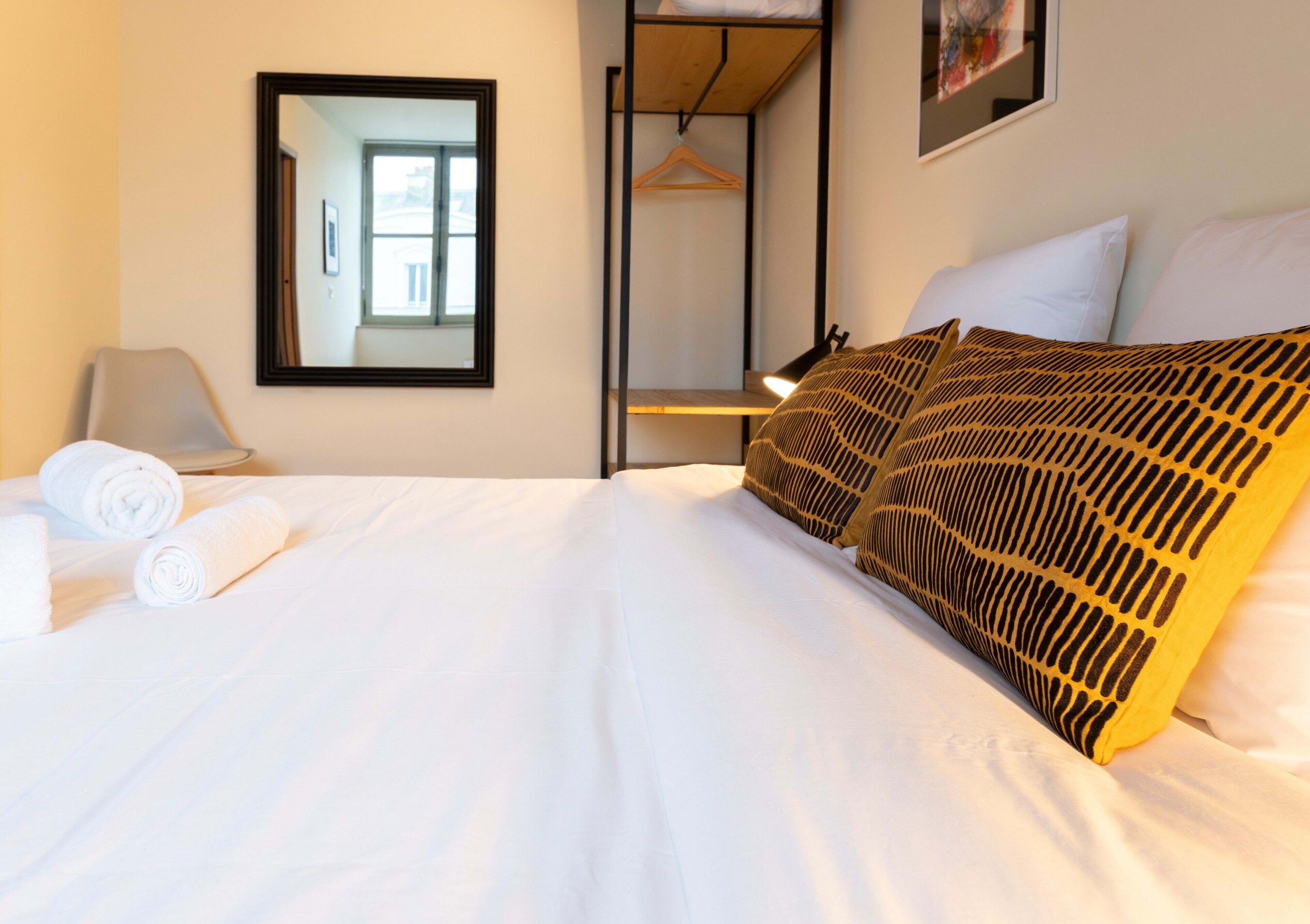 Ein Hotelzimmer mit Bett, Kleiderhaken, Spiegel und Fenster.