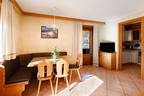 Ein gemütliches Zimmer mit einem Holzespeisetisch, Stühlen, einer Bank, einem Fernseher und einer Küchenzeile.