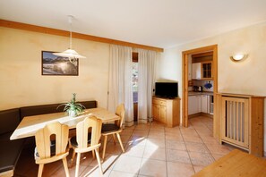 A dining area with a table and chairs, a television, and a kitchen area with wooden cabinets. - Apartment with Mountain View, Shared Garden and Wi-Fi (Livigno)