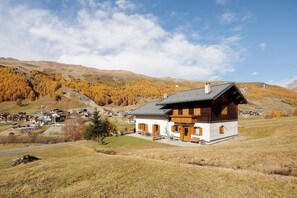 A mountain lodge with a sloped roof, wooden exterior, and a view of a valley with autumn trees.