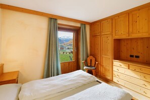 Ein Zimmer mit zwei Betten, Holzschränken, einem Stuhl und einem Fenster mit Blick auf die Berge.
