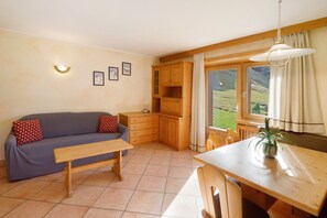 A cozy room with a sofa, wooden table, and cabinets, featuring a window with a view of greenery. - Apartment with Mountain View, Shared Garden and Wi-Fi (Livigno)