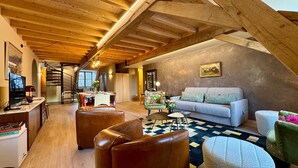 Um amplo loft com pé direito alto, vigas de madeira, área de refeições, sofá e escada.