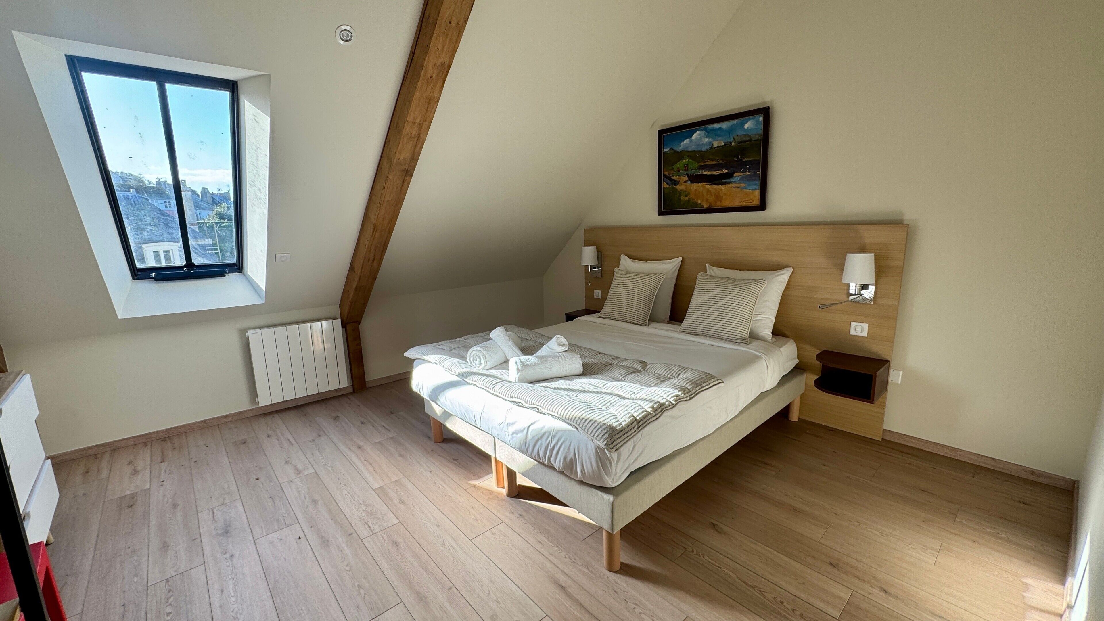 A bedroom with a bed, a window, a radiator, and a painting on the wall.