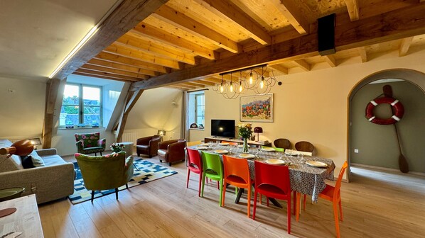 A dining area with a high ceiling and exposed beams, a television, and a painting on the wall.
