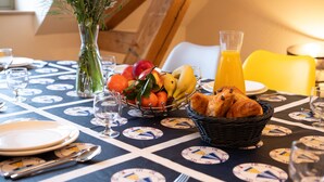 A breakfast table with plates, cutlery, a fruit bowl, a vase with flowers, and a glass of orange juice. - Apartment '7 - Seigneurie Fouquet' with Wi-Fi (Le Palais)