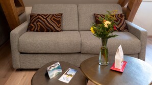 A grey sofa with patterned cushions, a small round table with a magazine and a vase with flowers, and a wooden chair in the background. - Apartment '7 - Seigneurie Fouquet' with Wi-Fi (Le Palais)