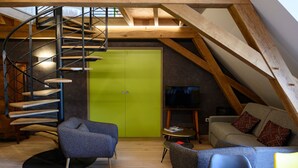 A loft-style room with a spiral staircase, a green door, a television, and a sofa with patterned cushions. - Apartment '7 - Seigneurie Fouquet' with Wi-Fi (Le Palais)