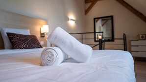 A neatly made bed with a rolled white towel, a patterned pillow, and a wall-mounted light fixture. - Apartment 'Seigneurie Fouquet - Tousquet' with Wi-Fi (Le Palais)