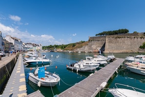Un port où des bateaux sont amarrés à un quai en bois, avec un mur de pierre et des bâtiments le long de la rive.