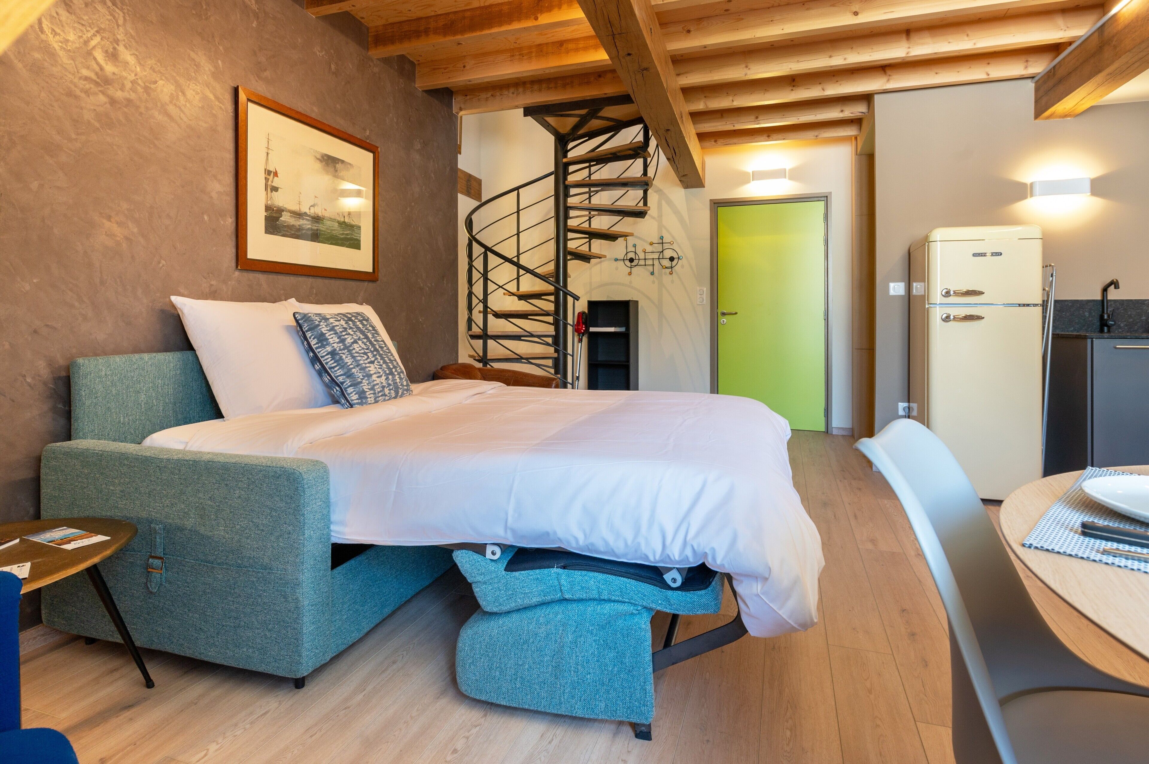 Een slaapkamer met een bed, een stoel, een tafel, een trap en een koelkast.