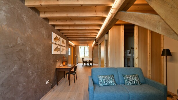A modern interior with a wooden ceiling, a blue sofa, a dining area, and a staircase.