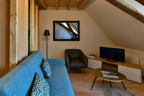 Una sala de estar moderna con un sofá azul, un sillón oscuro, una mesa de centro redonda y un televisor de pantalla plana sobre un mueble de madera.