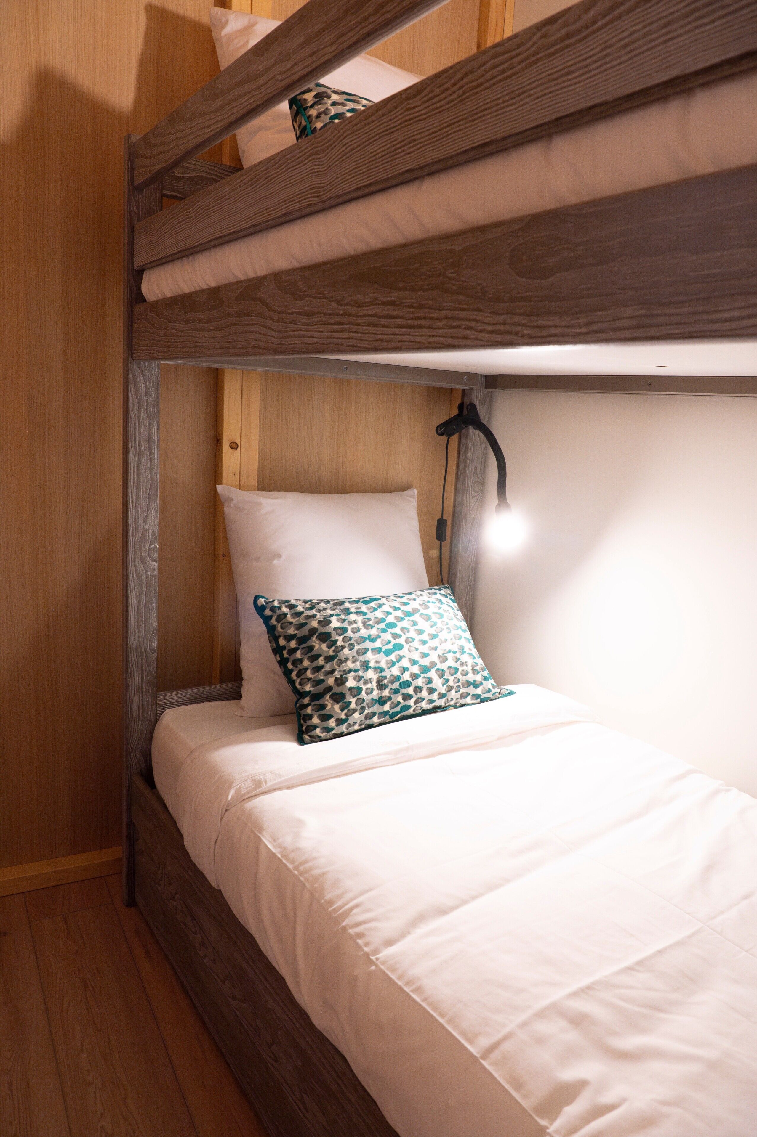 Un lit superposé avec une tête de lit en bois, un matelas blanc et un seul oreiller vert à motifs.