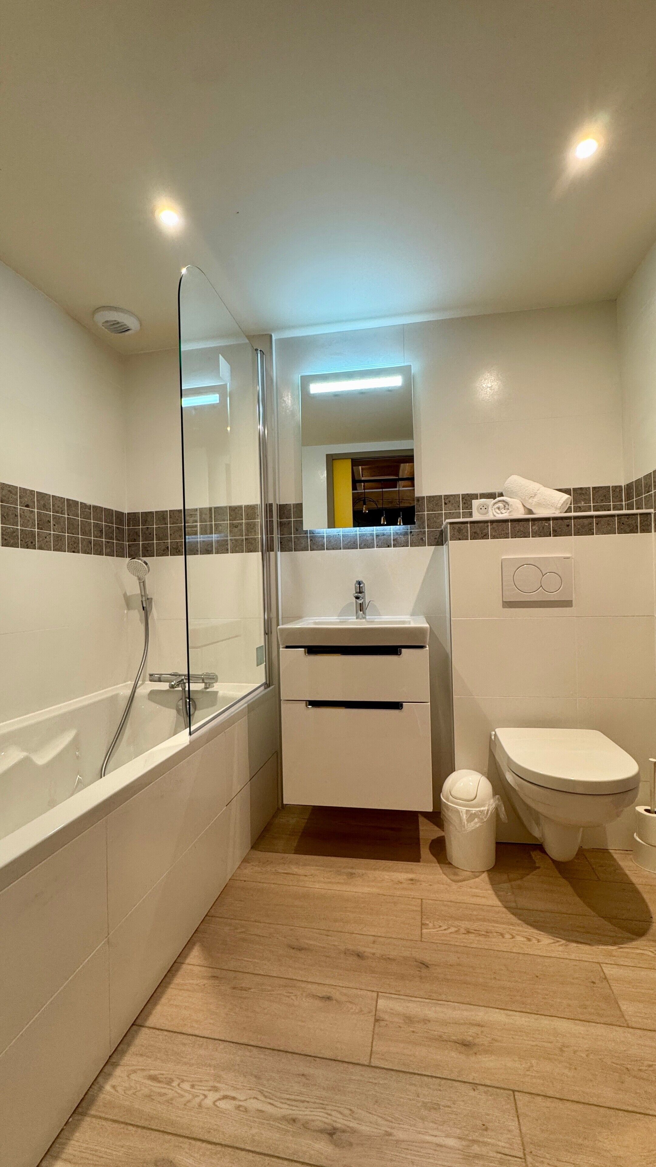 Ein modernes Badezimmer mit einer begehbaren Glasdusche, einem Waschbecken mit Spiegel, einer Toilette und einem Handtuchhalter.