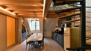 A modern kitchen with wooden beams, a dining area with a table and chairs, and a spiral staircase.