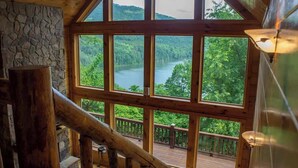 A wooden deck with a stone wall and large windows overlooking a lake surrounded by trees. - Lakefront Mountain Retreat on Watauga Lake (Butler)