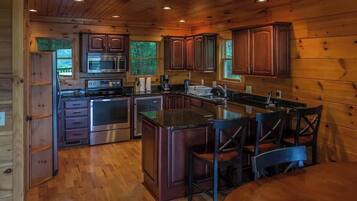 A wooden cabin interior with a kitchen featuring a stove, microwave, and cabinets.