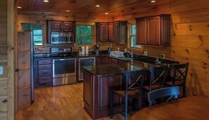 A wooden cabin interior with a kitchen featuring a stove, microwave, and cabinets.