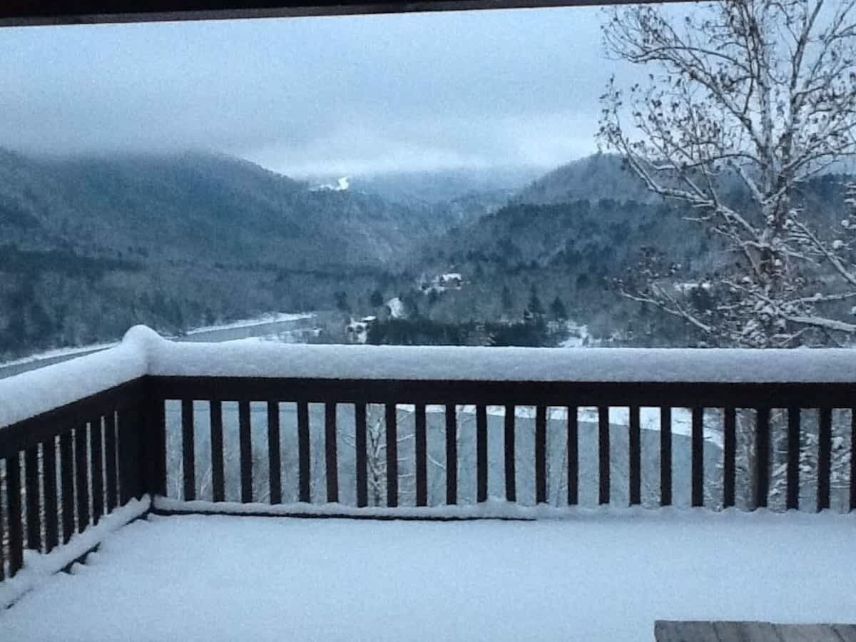 A snow-covered balcony with a view of a valley and mountains.