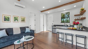 A modern kitchen with a central island, bar stools, and a dining area with a sofa and coffee table.