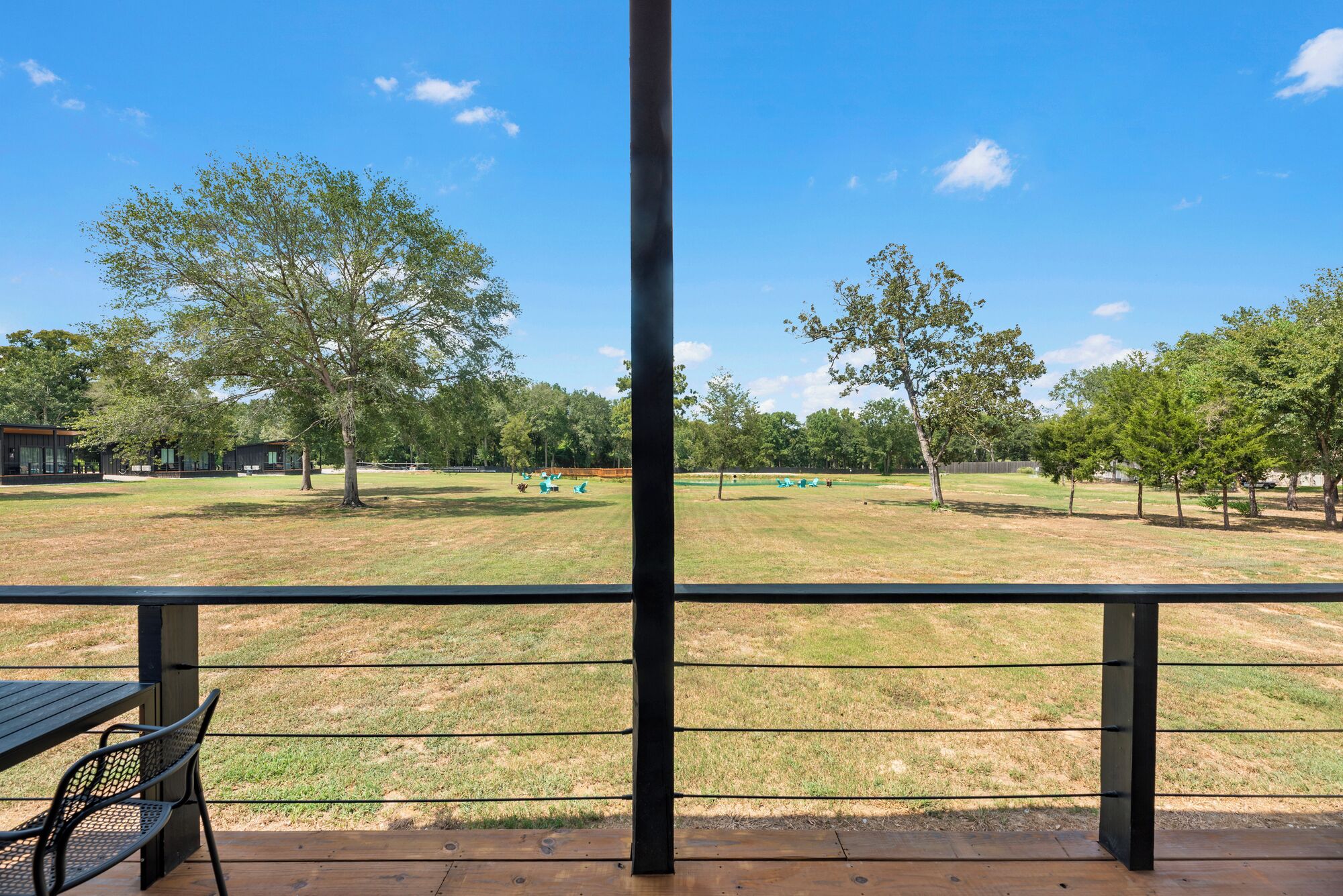 A view from a covered outdoor area with a wooden deck, metal railing, and a grassy field with trees.