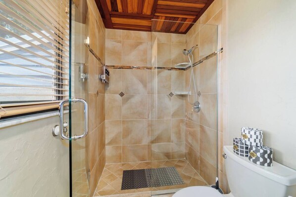 Un baño pequeño con cabina de ducha de vidrio, inodoro y ventana con persianas.