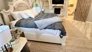 Een slaapkamer met een groot bed, een open haard, een plafondventilator en uitzicht op de badkamer.