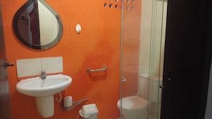 A bathroom with an orange wall, a white sink, a mirror, a toilet, and a glass shower enclosure. - OKAKOARAS HOTEL (Paulista)