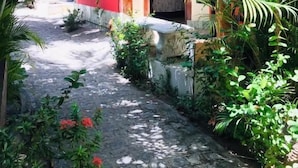 A narrow pathway leading to a building with a red and beige facade, surrounded by lush greenery and palm trees. - OKAKOARAS HOTEL (Paulista)