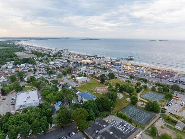 An aerial view of a coastal town with a beach, a pier, and a park with a basketball court.