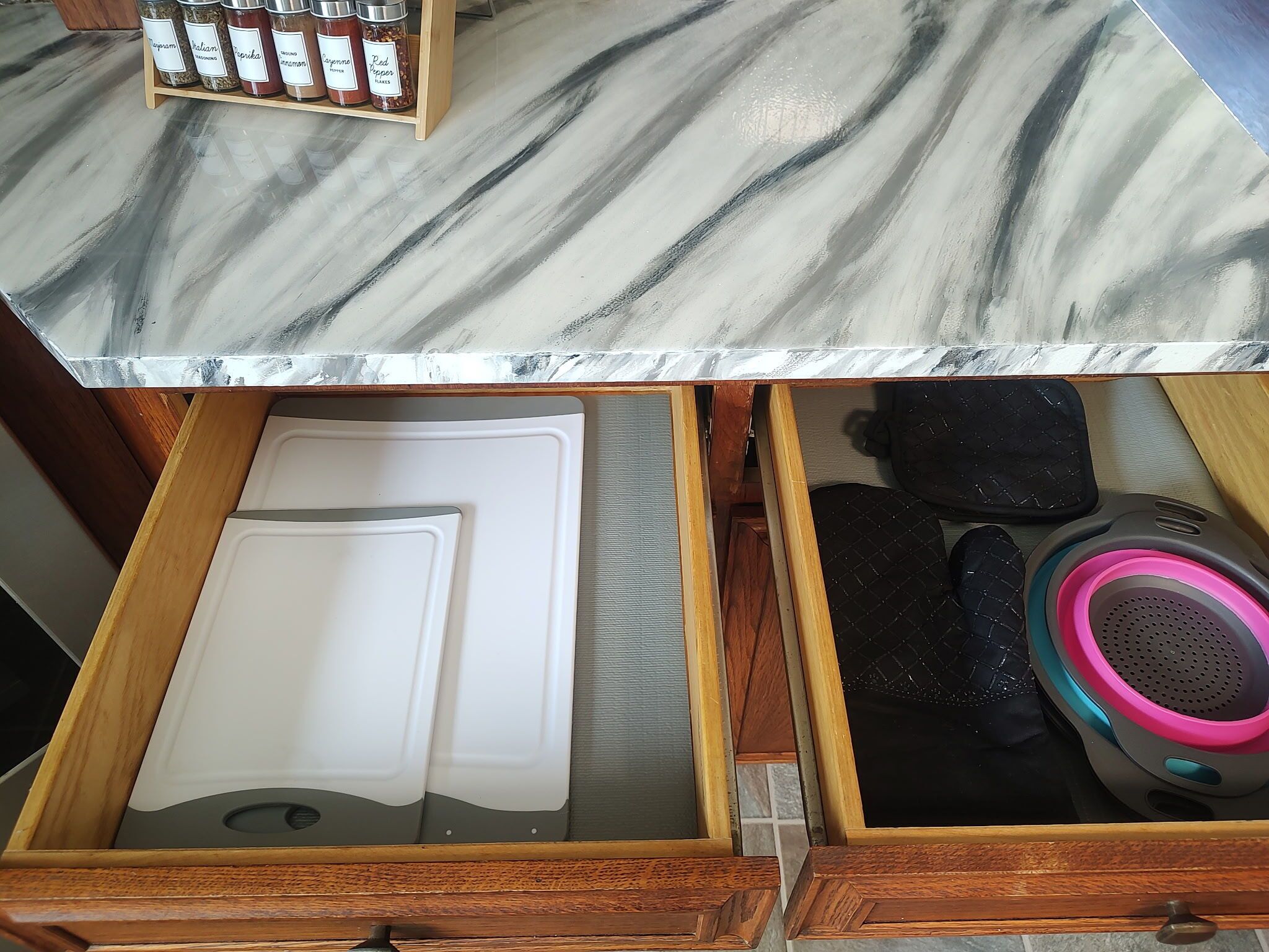 A kitchen counter with a marble top, a drawer with a white cutting board, and a black speaker with pink and blue accents.
