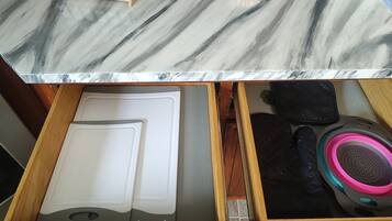 A kitchen counter with a marble top, a drawer with a white cutting board, and a black speaker with pink and blue accents.