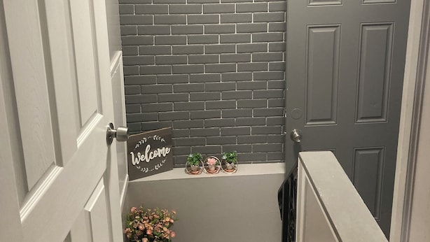 A staircase with a grey brick wall, a welcome sign, and small potted plants. - 2-bedroom House in beautiful Grand Island,NY! 4 miles from Niagara Falls! (Grand island)