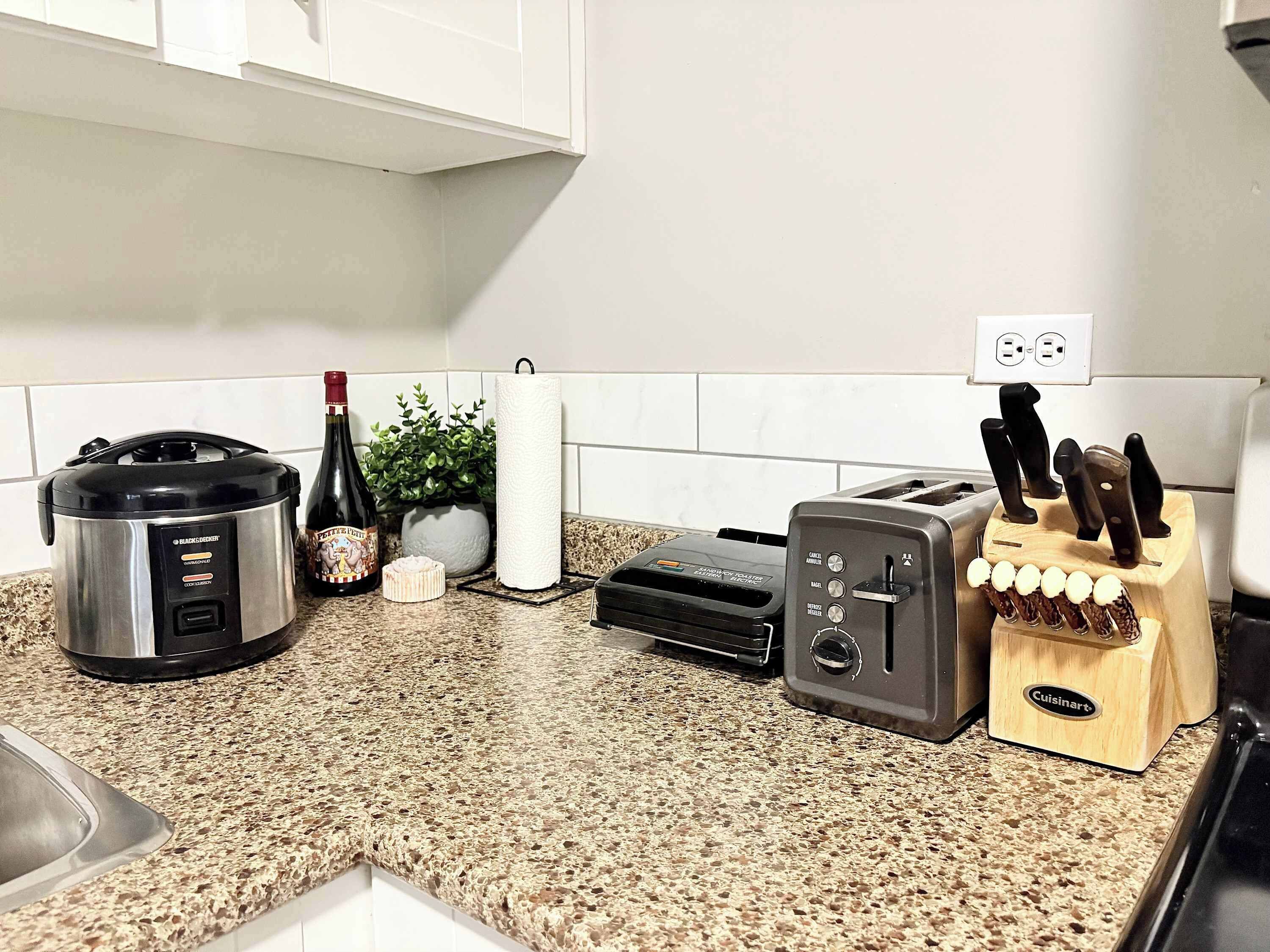 Una cocina con una olla de cocción lenta Black & Decker, un tostador, un bloque de cuchillos Cuisinart, una botella de vino y un rollo de toallas de papel.