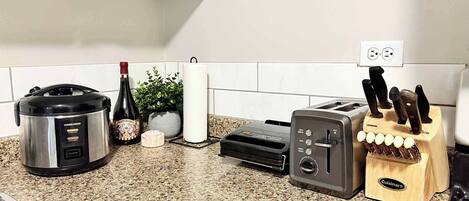 Una cocina con una olla de cocción lenta Black & Decker, un tostador, un bloque de cuchillos Cuisinart, una botella de vino y un rollo de toallas de papel.