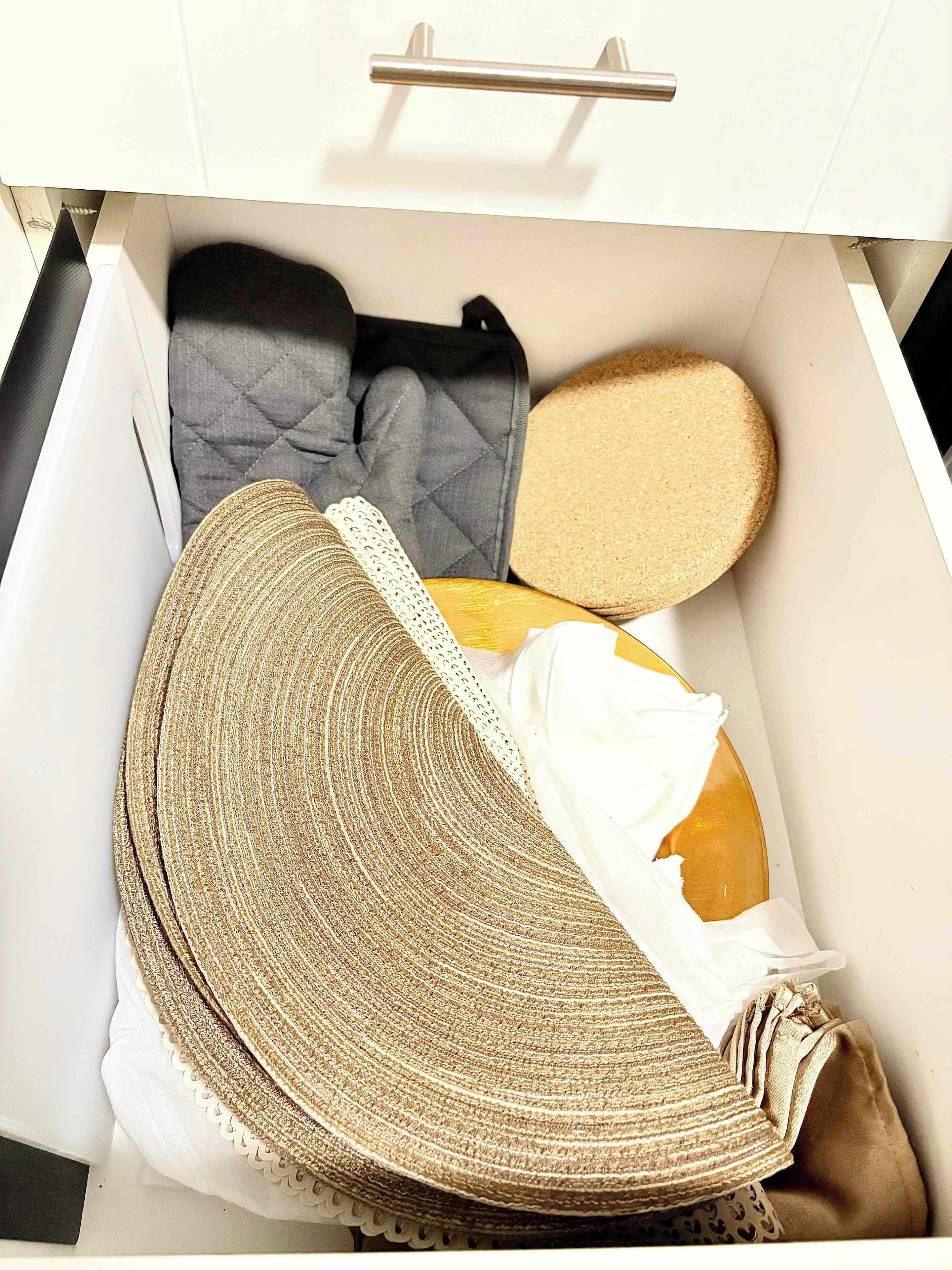A drawer with neatly organized items including a quilted bag, a round cushion, and folded blankets.