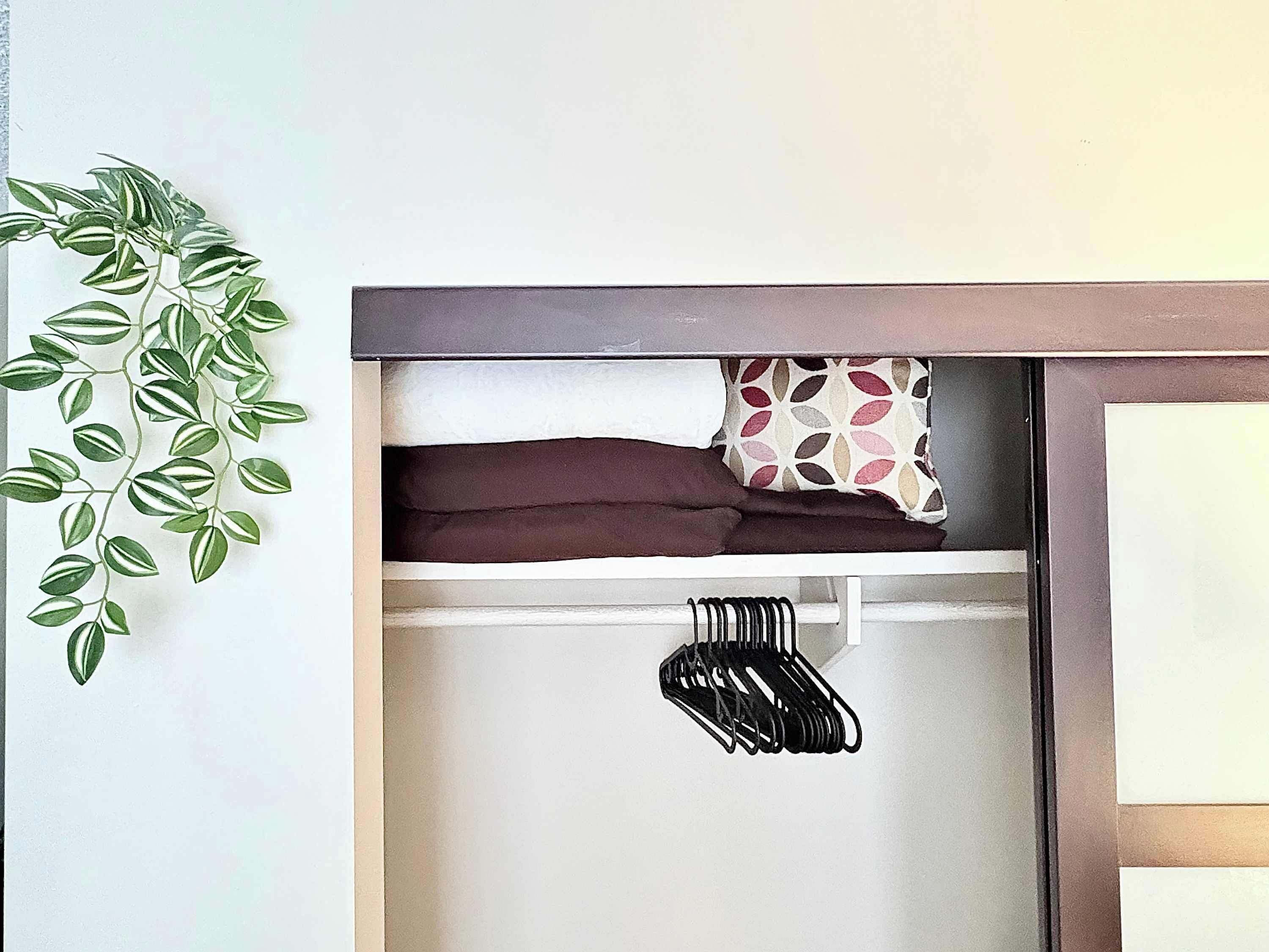 Ein Schlafzimmer mit einem Bett, einem Kissen, einer hängenden Pflanze und einem Kleiderständer.
