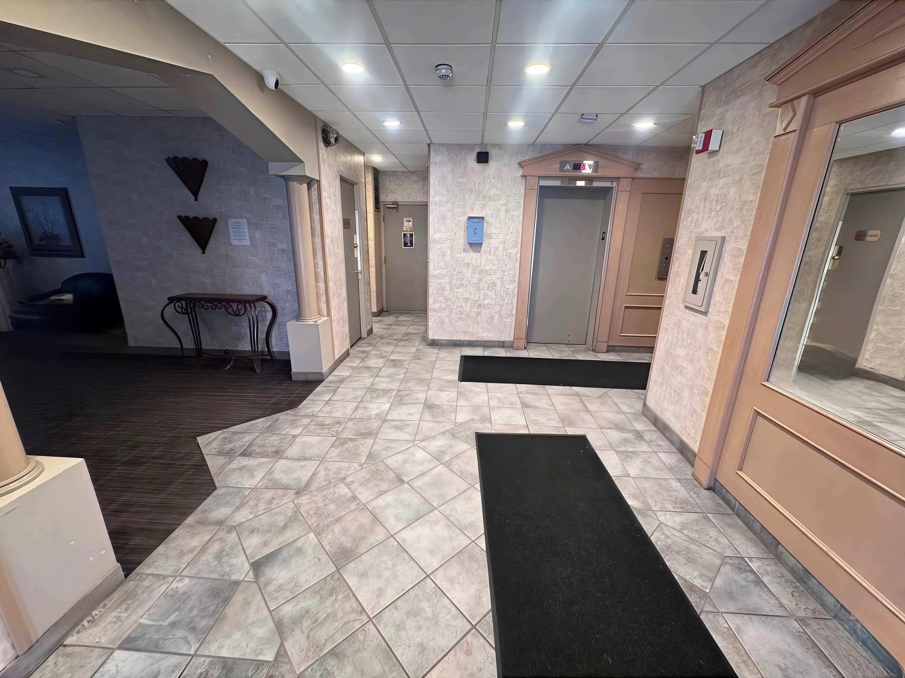 A hotel lobby with a tiled floor, a reception desk, a staircase, and an elevator.