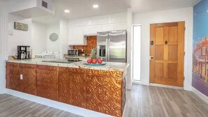 Une cuisine moderne dotée d’un îlot central aux motifs cuivrés, d’appareils électroménagers en acier inoxydable et d’une porte en bois.