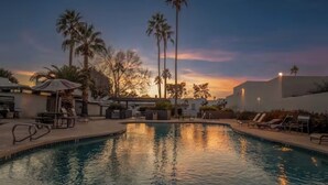 Une piscine avec des chaises longues et des palmiers, au coucher du soleil.