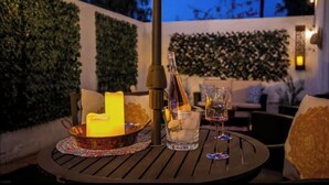 Un espace extérieur aménagé avec une table ronde, des bougies, une bouteille et des verres.