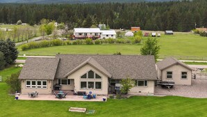 A two-story house with a patio area, a large window, and a garage. - New! Home on one acre, dog friendly, private hot tub (Kalispell)