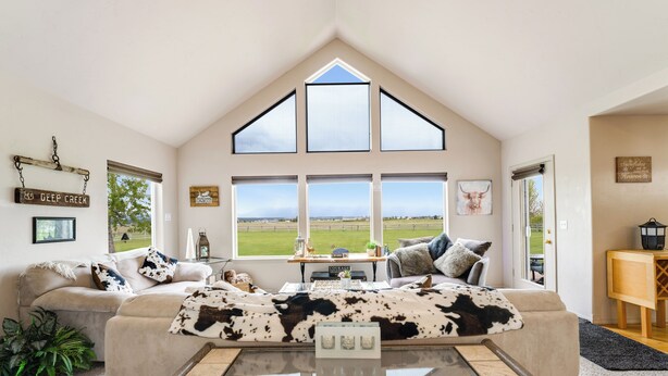 A spacious living room with a high ceiling, large windows, a cozy sofa, and a glass coffee table. - New! Home on one acre, dog friendly, private hot tub (Kalispell)