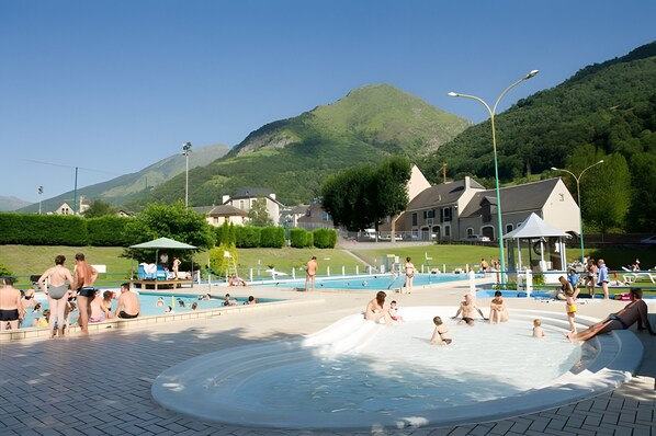 A swimming pool area with a water slide, surrounded by houses and a mountain in the background.